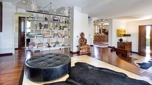 A spacious living room with a large bookshelf, a leather ottoman, and a statue.