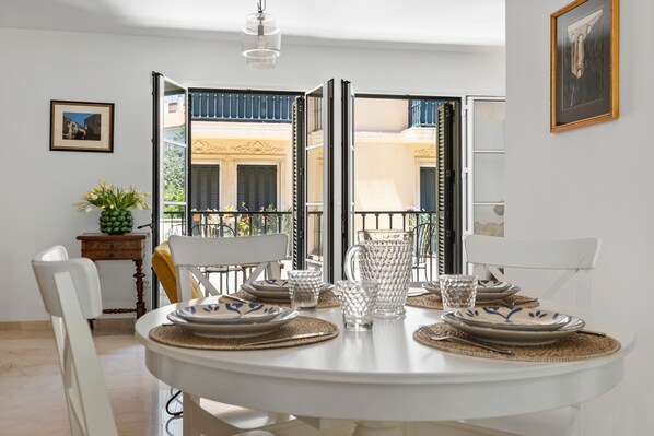 A dining area with a round table set for two, a potted plant, and a view of the outside balcony.
