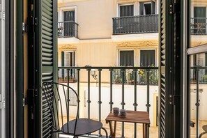 A balcony with a chair and a table, overlooking a building with balconies and windows.