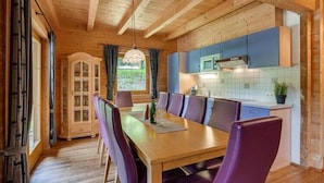 Un interno in legno con un tavolo e sedie da pranzo, una cucina con mobili blu e una finestra con tende.