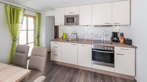 Une cuisine moderne avec des meubles blancs, un four à micro-ondes, un évier et une cuisinière. On y trouve une table à manger avec des chaises et une fenêtre ornée de rideaux verts.
