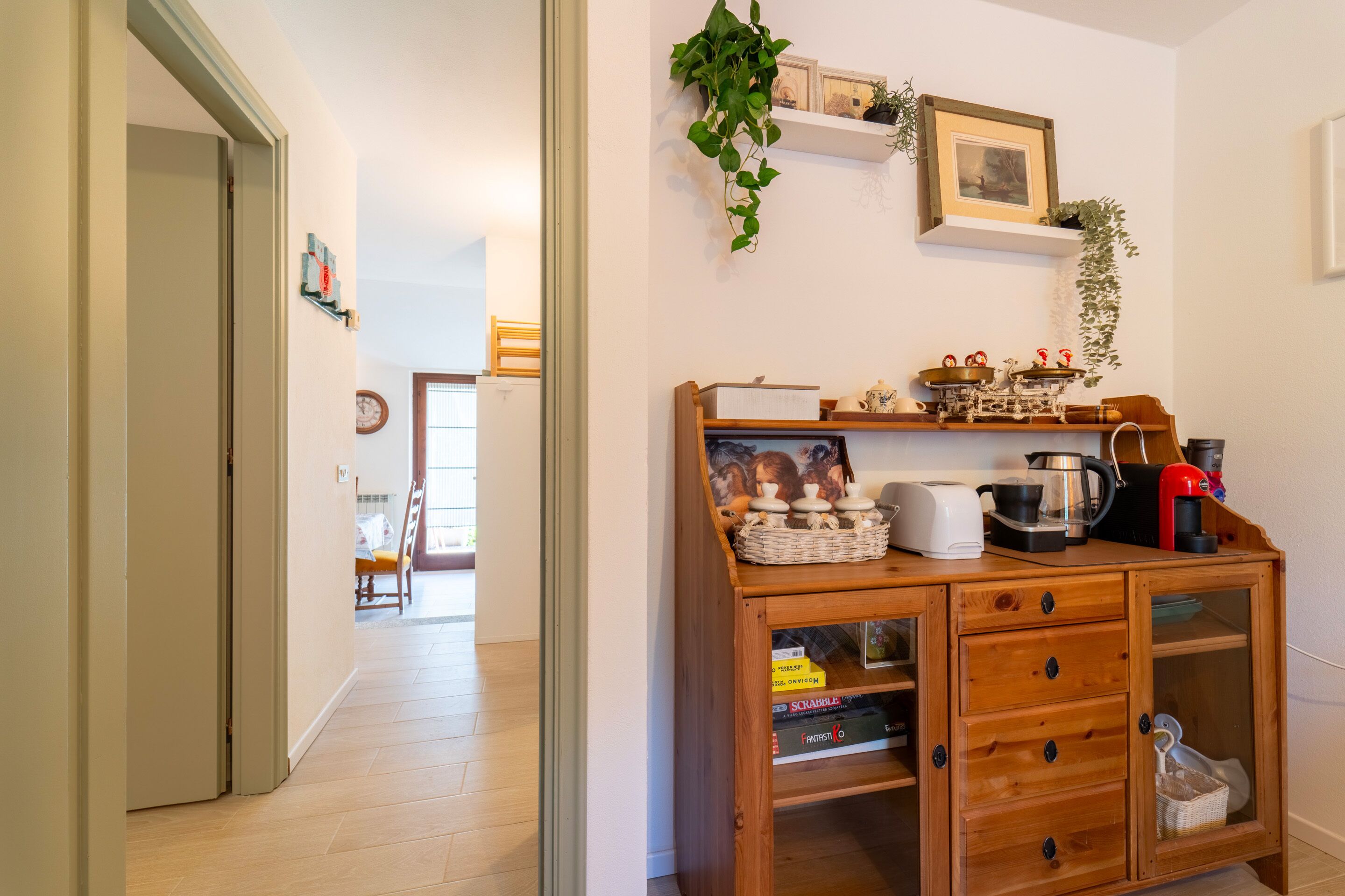 Un meuble en bois avec des tiroirs et des étagères, une plante suspendue et un tableau encadré au mur.