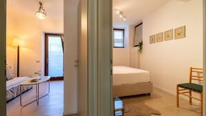 Un dormitorio con cama, una silla, una mesita, una lámpara y una ventana.