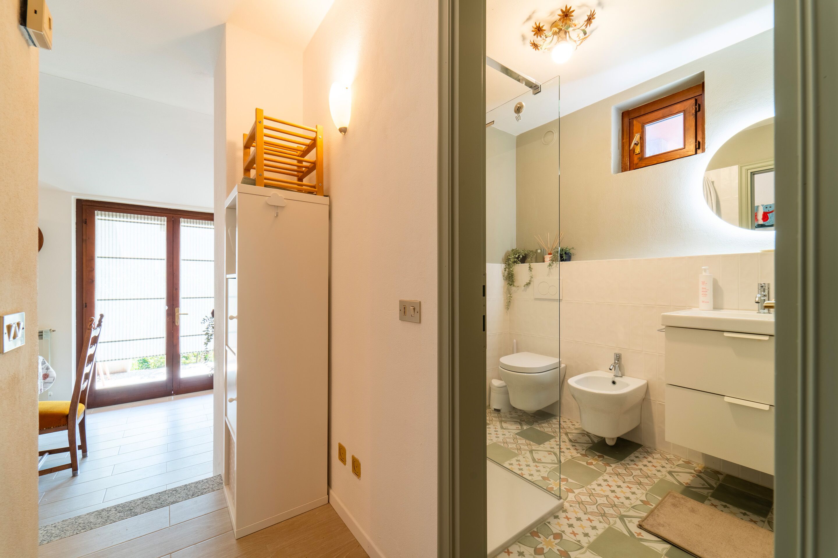 A modern bathroom with a toilet, bidet, and sink. There is a small window above the toilet and a mirror on the wall.