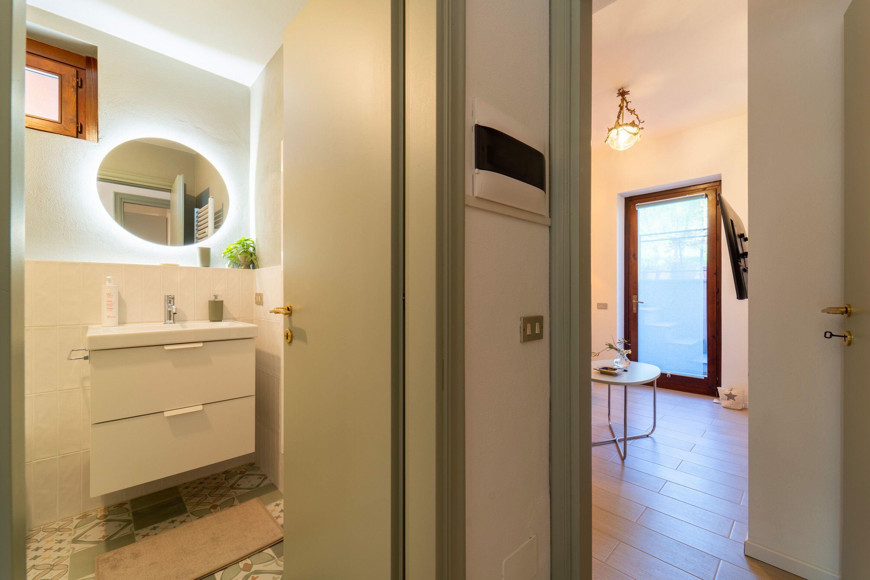 Une salle de bain moderne avec un meuble-lavabo blanc, un miroir rond et une petite plante.