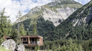 Eine Bergingerhütte mit Balkon, umgeben von dichtem Wald und einem markanten Berg im Hintergrund.
