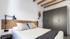 A modern bedroom with a wooden headboard, a bed with patterned bedding, a bedside table, a desk lamp, and a wardrobe. - Unik Vacation Alt Camp (Puigpelat)