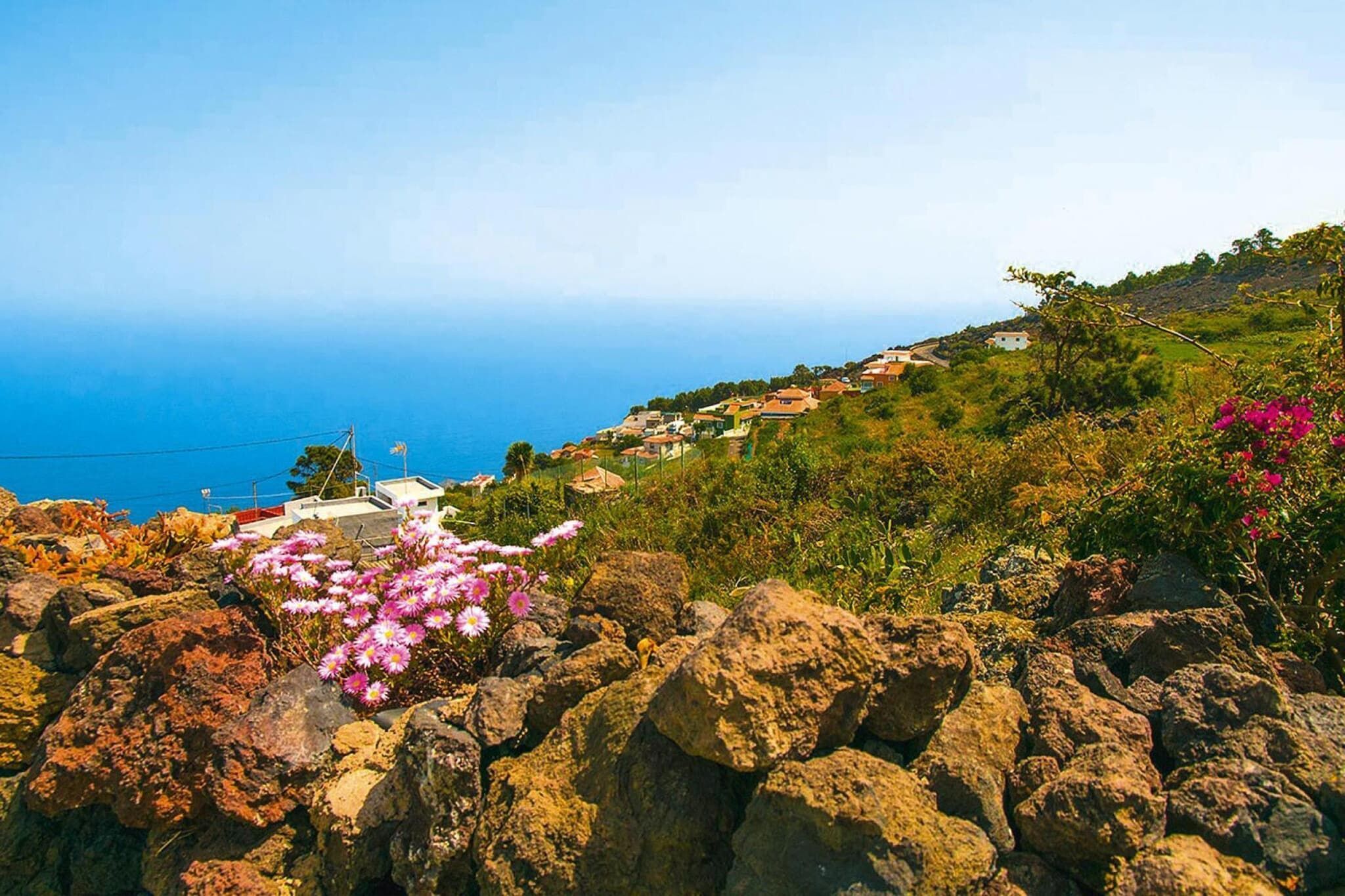 A coastal landscape with a view of the sea, rocky terrain, and a cluster of buildings.