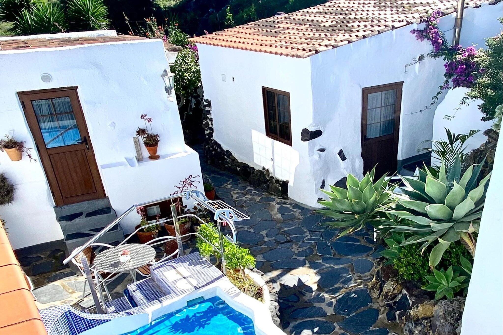 A courtyard with a pool, white buildings, and potted plants.