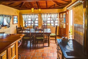 A rustic kitchen with a wooden table, chairs, a stove, and a window with curtains.