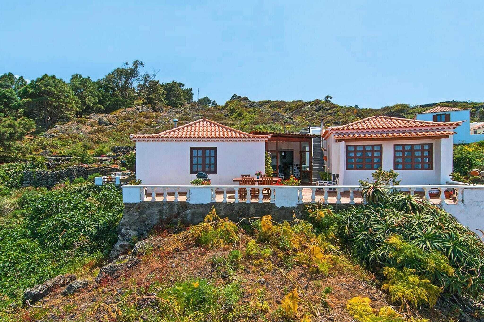 A two-story house with a balcony, surrounded by vegetation and hills.