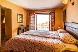 A bedroom with a bed, a nightstand, a window with curtains, and a view of the outside.