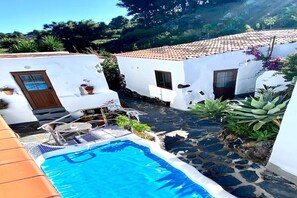 Una zona de piscina con techo de baldosas, paredes blancas y plantas en macetas.