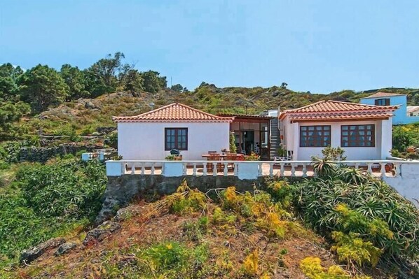 Una casa de dos pisos con techo de tejas, un balcón y vistas a un paisaje montañoso.
