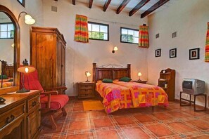 Un dormitorio con una cama de madera, dos mesitas de noche con lámparas, un armario, un televisor y una ventana con cortinas.
