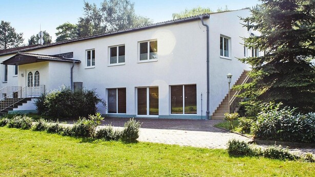 Ein zweistöckiges Gebäude mit weißer Fassade, einer Veranda und einer Treppe, die zu der oberen Etage führt.