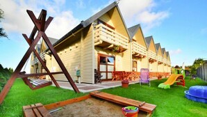 Eine Reihe Holzhütten mit Balkonen, ein Spielplatz und ein Sandspielbereich.