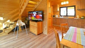 Innenansicht einer Holzhütte mit Essbereich, Küche und Fernseher im Wohnbereich.