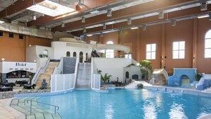Una piscina interior con zona de bar, toboganes y una escalera que lleva a un nivel superior.