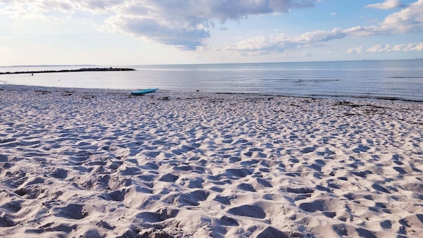 A sandy beach with footprints leading to the water, a distant pier, and a partly cloudy sky.