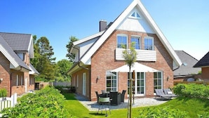 A modern two-story house with a brick exterior, a covered patio with outdoor furniture, and a well-maintained garden.