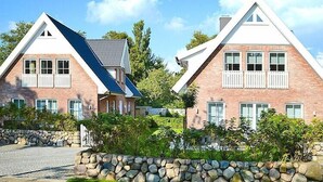 Two brick houses with gabled roofs and white railings, surrounded by greenery and a stone wall.