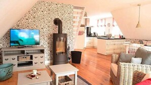 A cozy living room with a TV, a fireplace, a kitchen in the background, and a dining area.