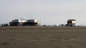 Une plage avec deux constructions en bois, l’une plus grande, avec une enseigne, et l’autre plus petite.