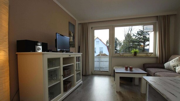 Un salon comprenant un téléviseur, des meubles de rangement, un canapé et une fenêtre donnant sur une maison et des arbres.