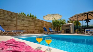 A swimming pool with lounge chairs and umbrellas, a wooden fence, and a barbecue area. - Jokos House in Roda With 2 Bedrooms and 2 Bathrooms (Corfu)