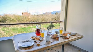 A breakfast table with food and drinks on a balcony overlooking a grassy area and mountains. - Jokos House in Roda With 2 Bedrooms and 2 Bathrooms (Corfu)