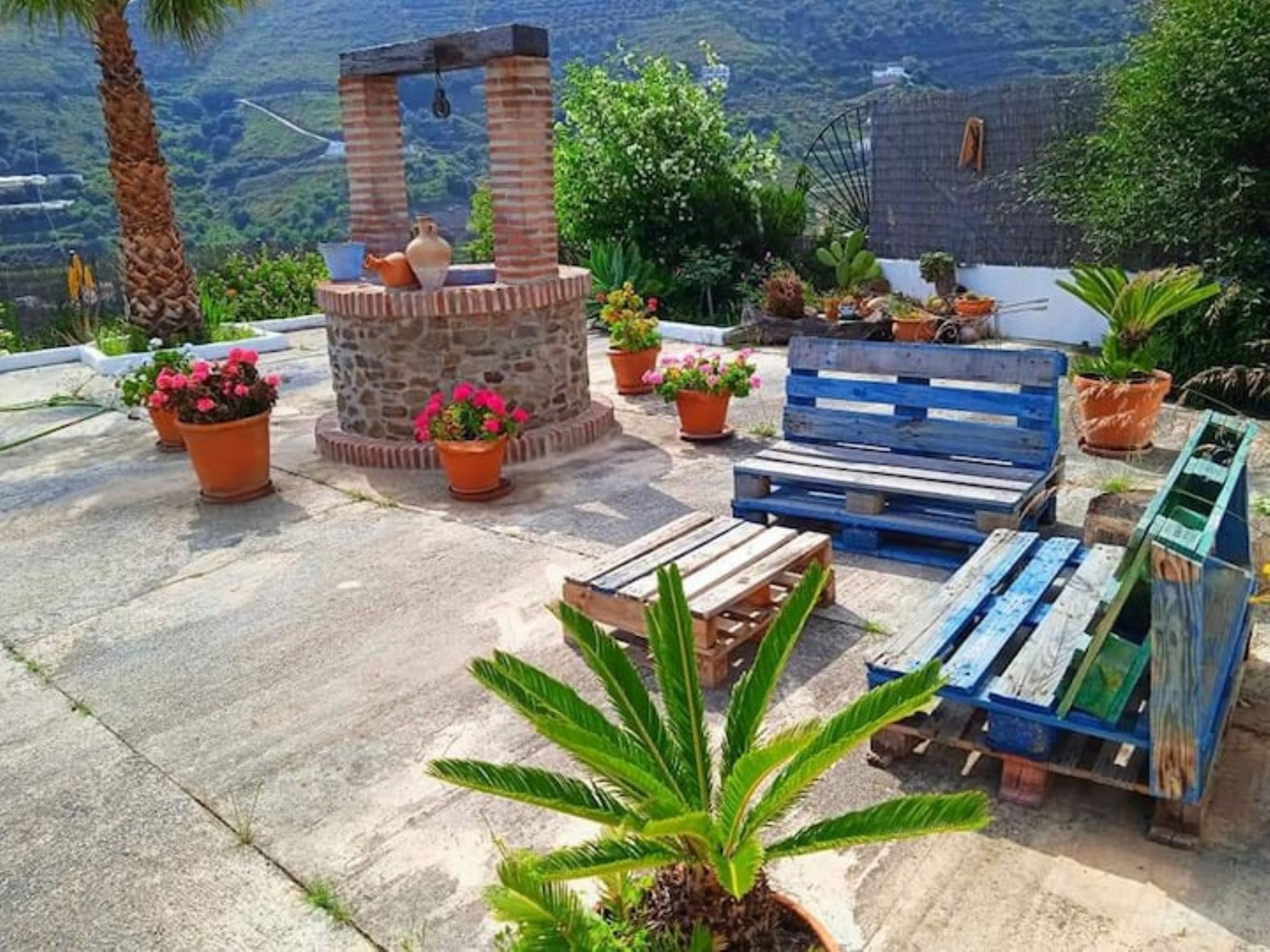 A patio with a stone fountain, wooden benches, and potted plants.