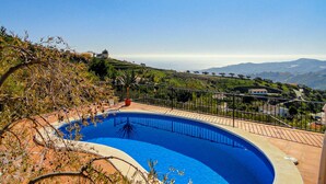 Une piscine à bord incurvé, entourée d’une terrasse carrelée et d’un garde-corps en métal.