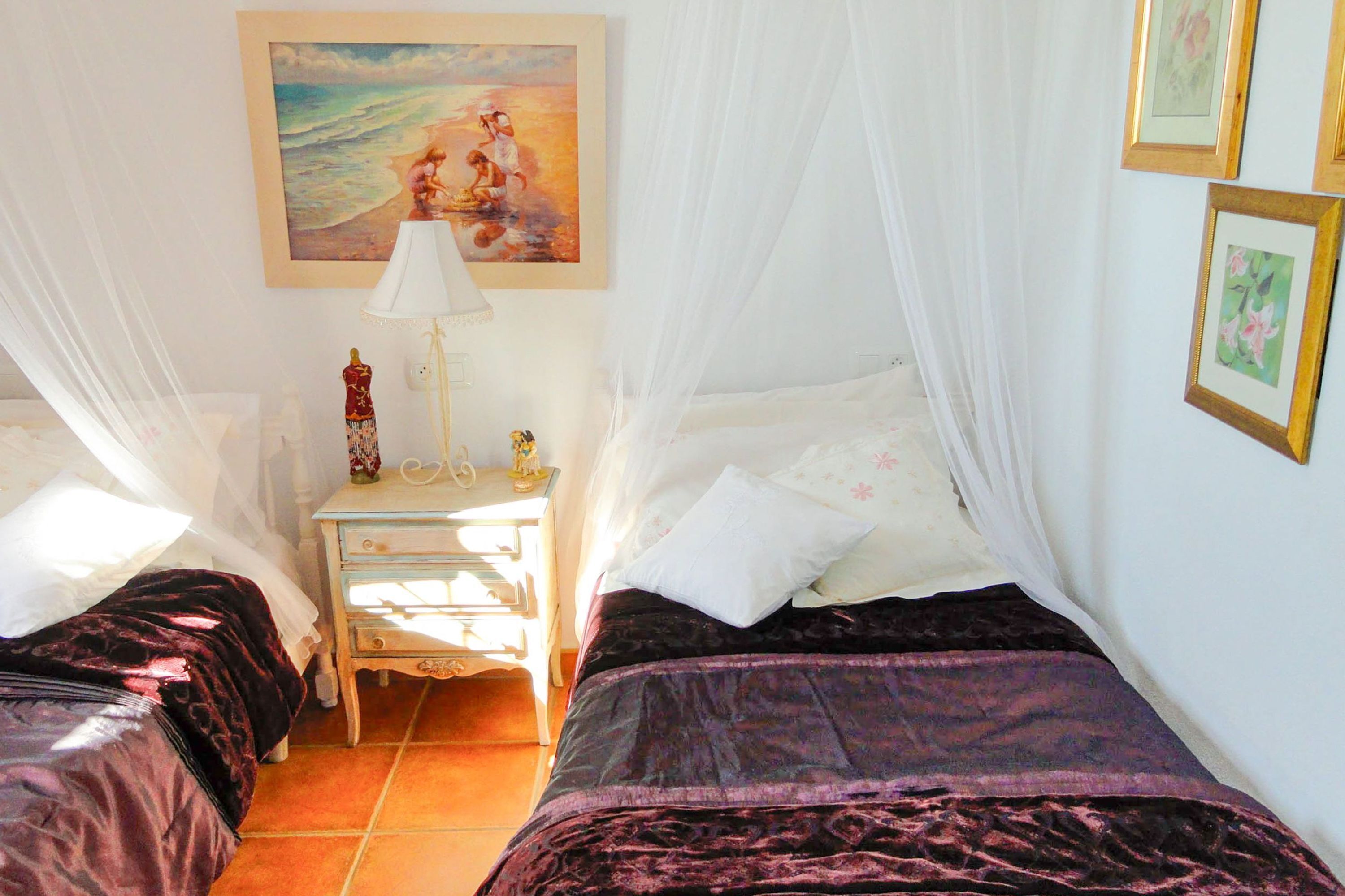 A room with two beds, a nightstand, a lamp, and a painting on the wall.