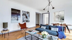 Un salon moderne avec un canapé bleu, un fauteuil rouge et une table basse sur laquelle on trouve des magazines et un vase de fleurs.