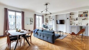 Un salon moderne comprenant un canapé, une table à manger, des chaises et un téléviseur fixé au mur.