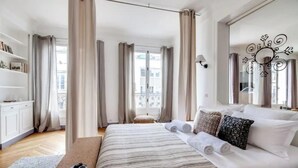Une chambre moderne avec un grand lit, une table de chevet, une bibliothèque et une fenêtre avec des rideaux.