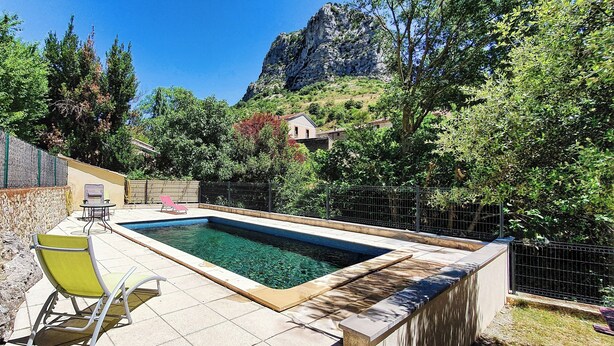 Piscina com parede de pedra e uma cadeira, cercada por árvores e uma montanha ao fundo.