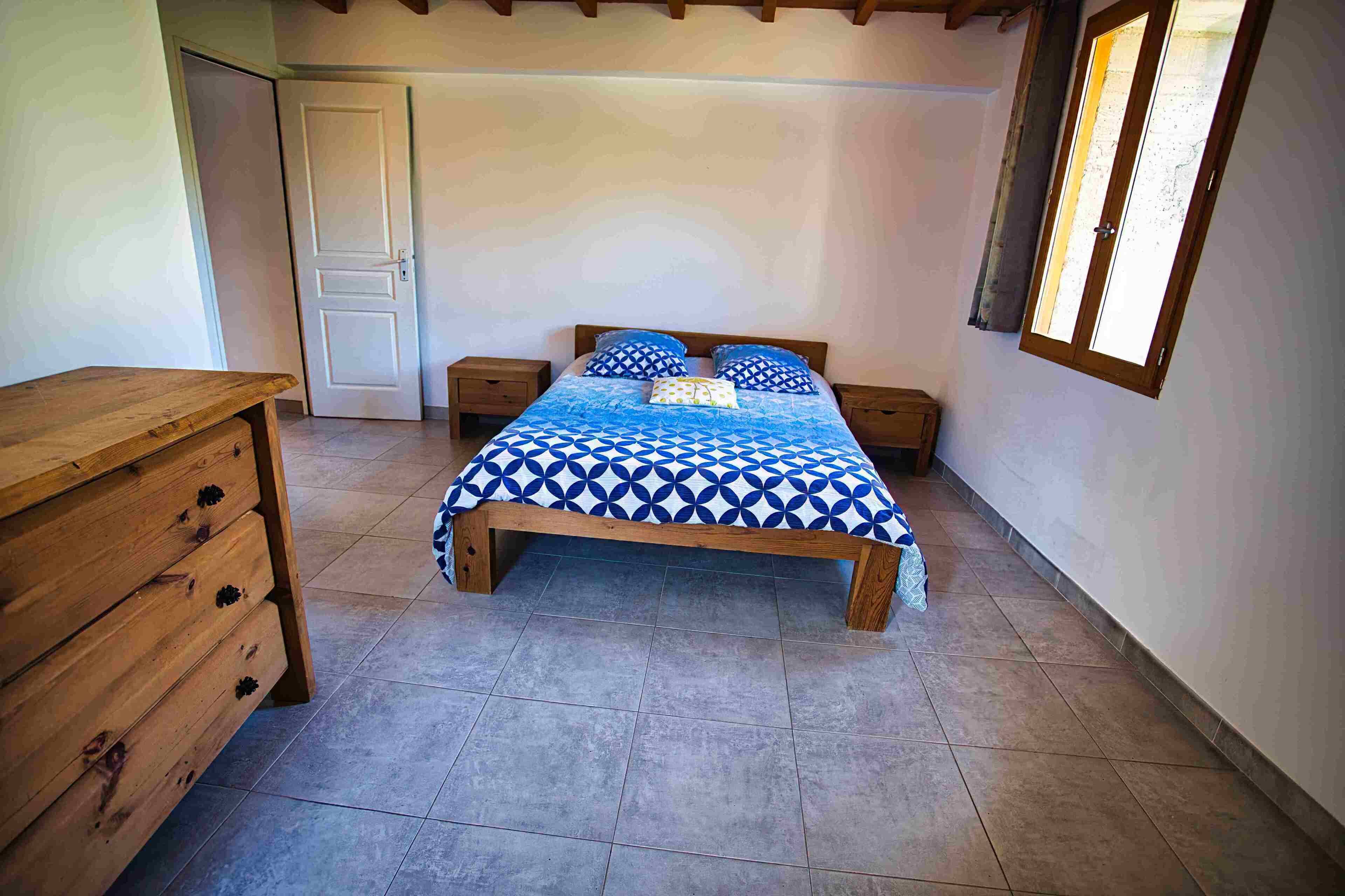A bedroom with a wooden bed, two bedside tables, a wooden dresser, and a window with curtains.