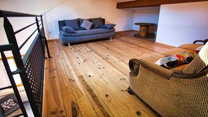 Quarto estilo loft com piso de madeira, um sofá, uma poltrona e uma pequena mesa.