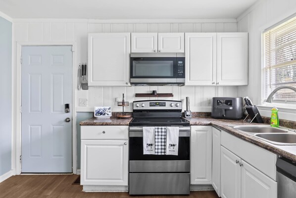 A kitchen with white cabinets, a stainless steel oven, a microwave, and a sink.