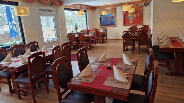 A restaurant with wooden tables and chairs, red placemats, and a large window with a view of trees. - PB Hotel Pension (Goslar)