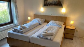 A double bed with two pillows and a folded towel on each side. There is a nightstand with a lamp on the right. - PB Hotel Pension (Goslar)