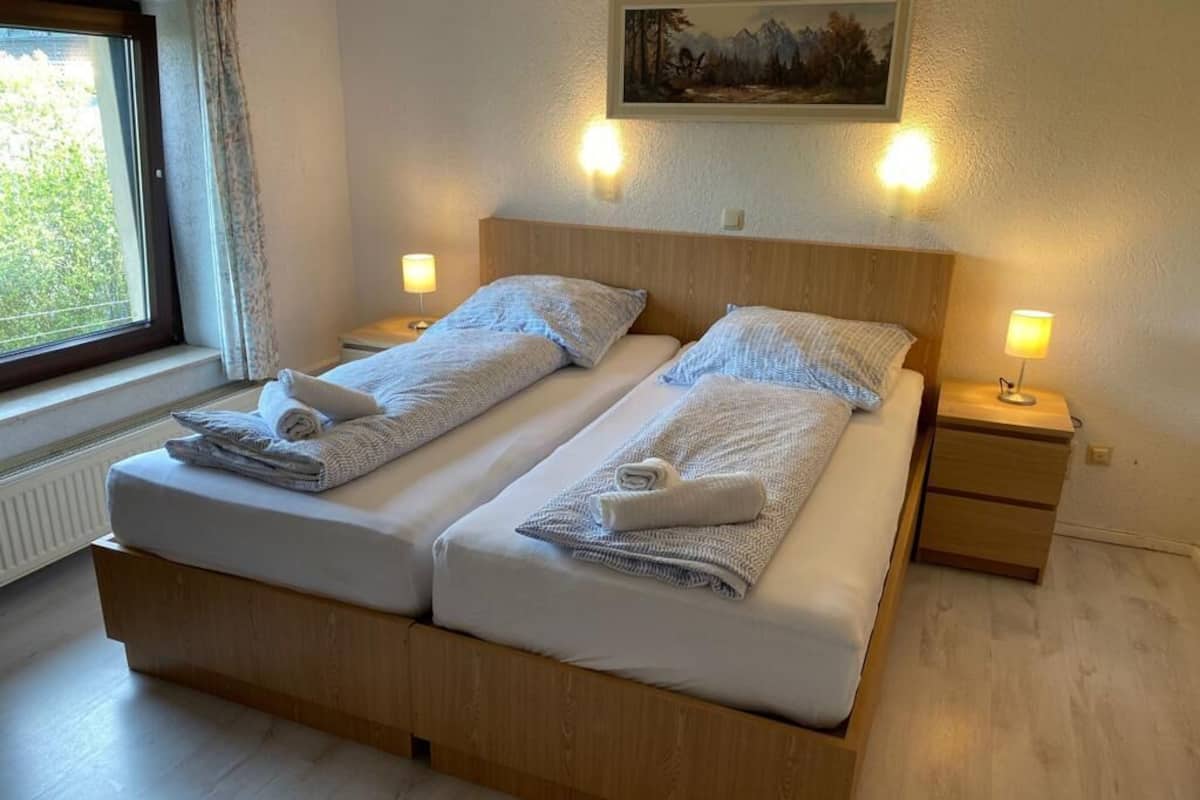 Un lit double avec deux oreillers et une serviette pliée de chaque côté. Il y a une table de chevet avec une lampe sur le côté droit.