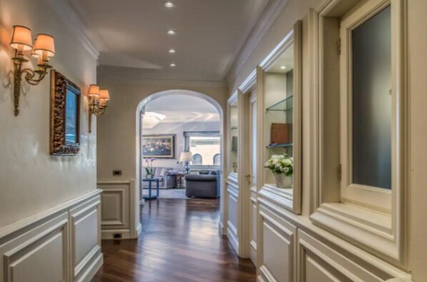 A hallway with a wooden floor, white walls, and a large arched doorway leading to a living area with furniture and a view of the cityscape. - 
Luxurious Apartment Overlooking the Colosseum  (Roma)