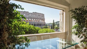 A room with a glass table and chairs, a window with a view of the Colosseum, and indoor plants. - 
Luxurious Apartment Overlooking the Colosseum  (Roma)