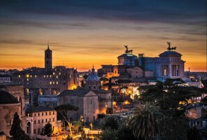 A cityscape at dusk with prominent historical architecture, including a bell tower and a domed building.