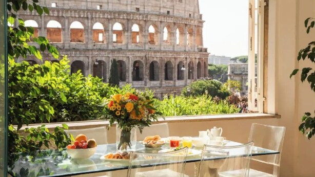 A dining table with a view of the Colosseum, clear glass chairs, and a vase of flowers. - 
Luxurious Apartment Overlooking the Colosseum  (Roma)
