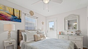Un dormitorio con cama, mesita de noche, lámpara y un cuadro grande en la pared.
