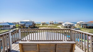 Una terraza de madera con vista a una zona de playa con varias casas y un cielo despejado.